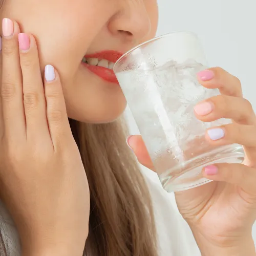 Woman holding jaw in pain as she drinks water from glass.