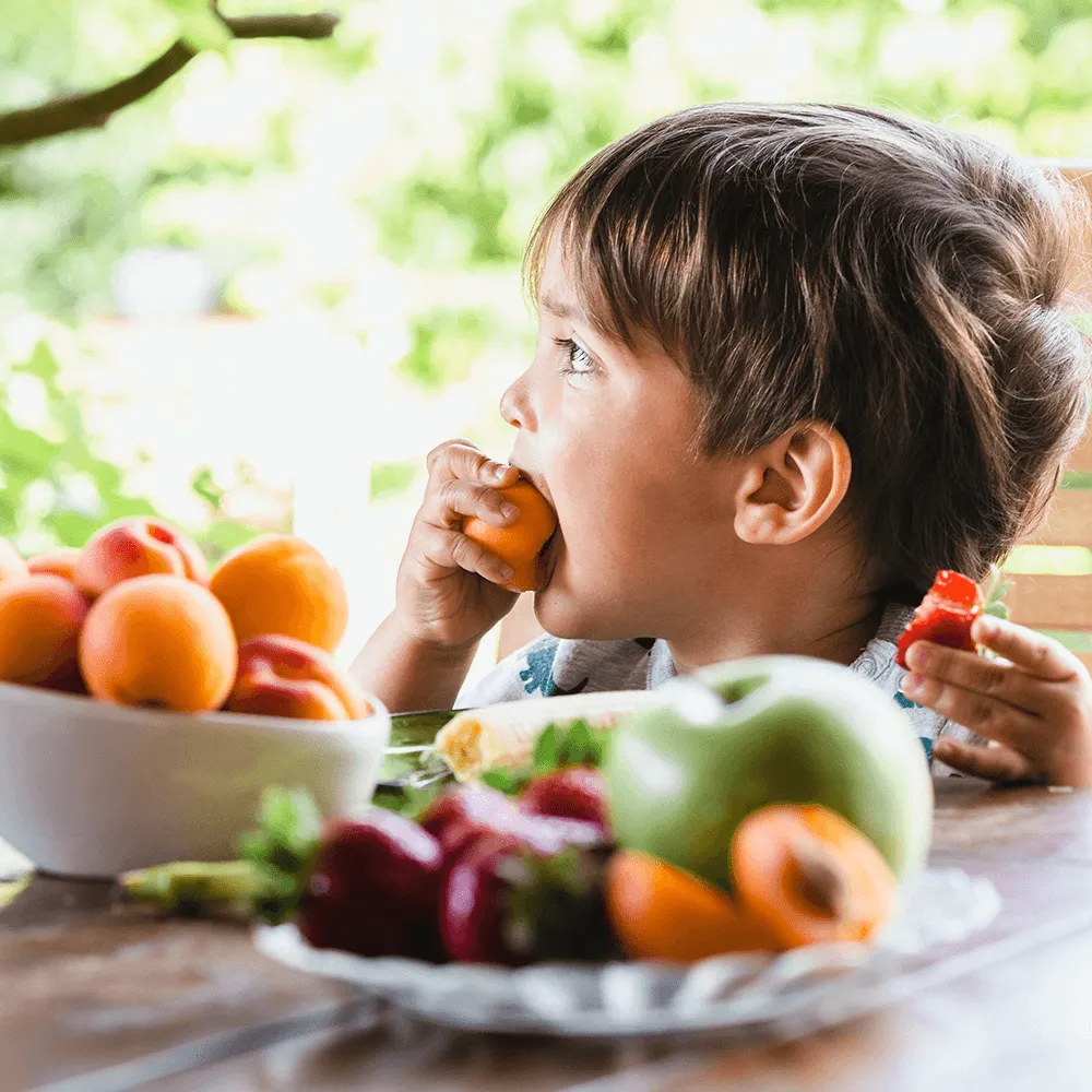 Toddler happily eating apricots and strawberries outdoors.