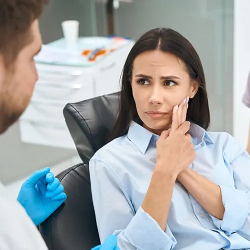 Female patient holding her cheek and looking at male dentist.