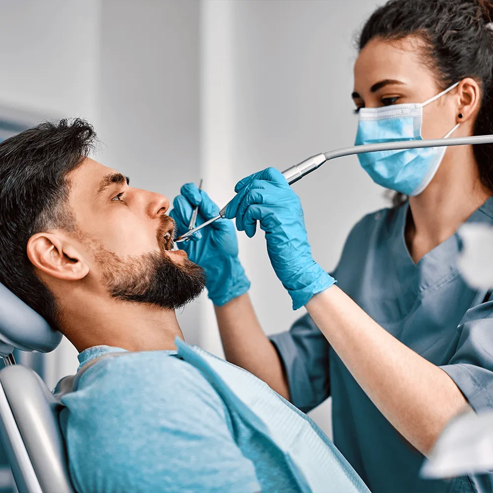 Dentist using dental tools to examine a male patient's teeth.