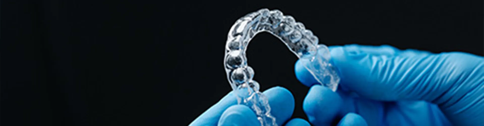 Gloved-hands holding clear aligner.