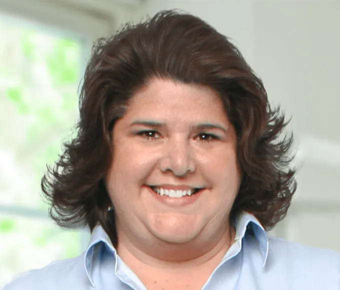 Headshot of smiling woman with shoulder-length brown hair, wearing a light blue shirt.