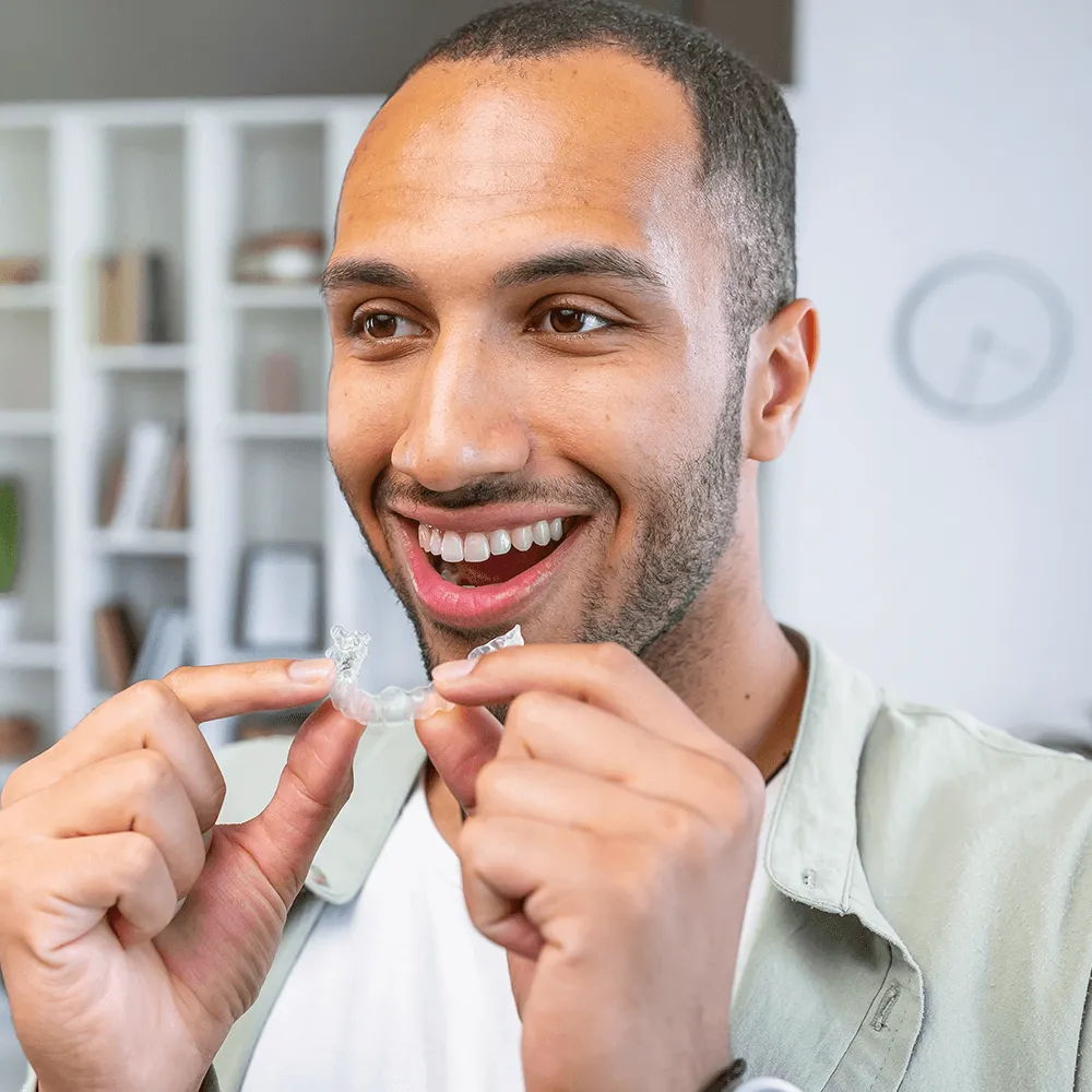 Man smiling and holding clear Invisalign aligners.