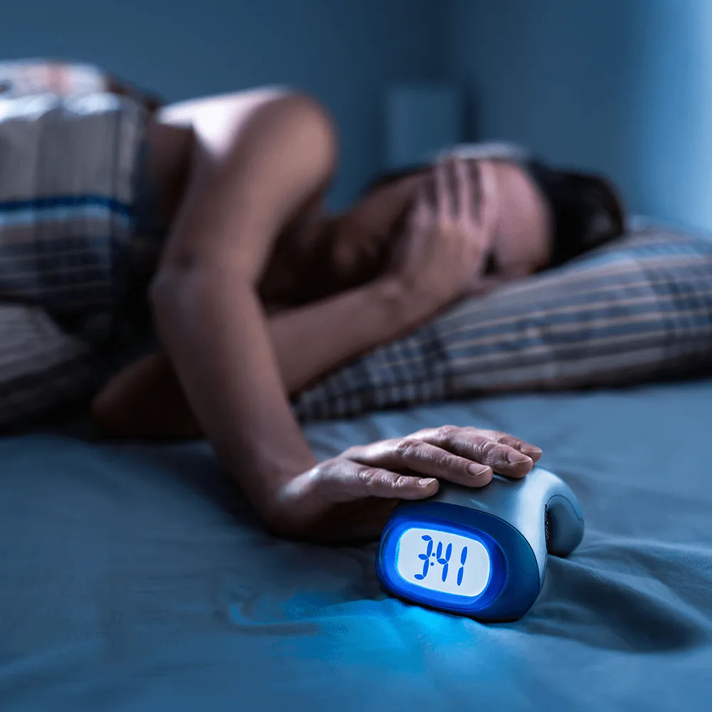 Woman awake at 3:41 AM, hand on digital alarm clock, showing insomnia.