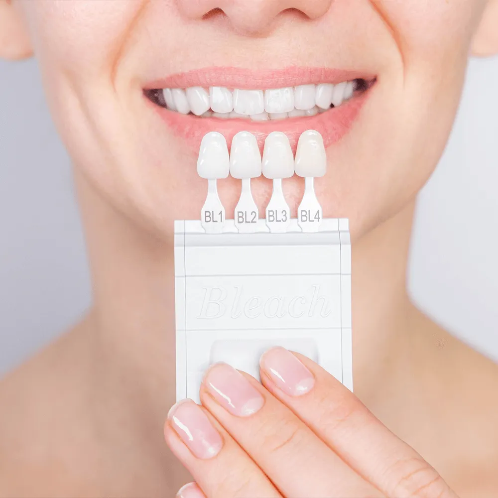 Woman holding teeth whitening shade guide, showing bleached teeth.  Shades BL1-BL4.