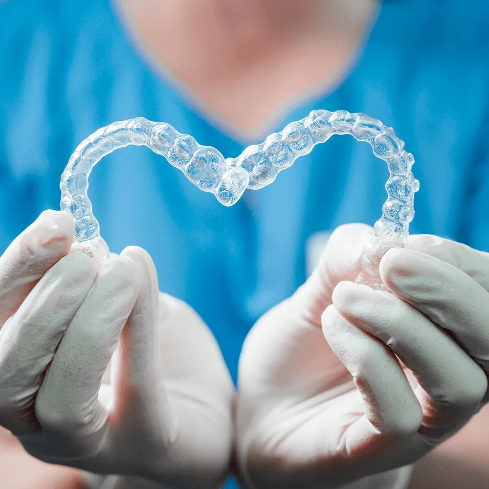 Dentist's hands in gloves hold clear Invisalign aligners.