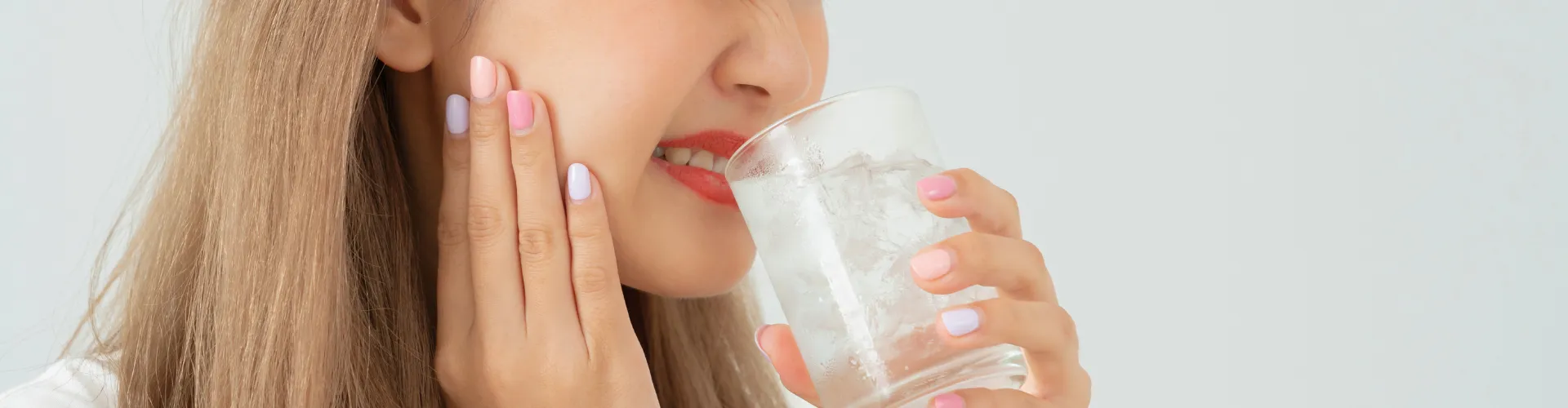 Woman holding jaw in pain as she drinks water from glass.