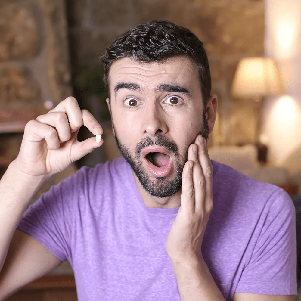 Shocked man holding lost tooth, jaw pain.