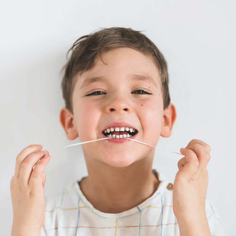 Smiling child flossing teeth with white shirt.