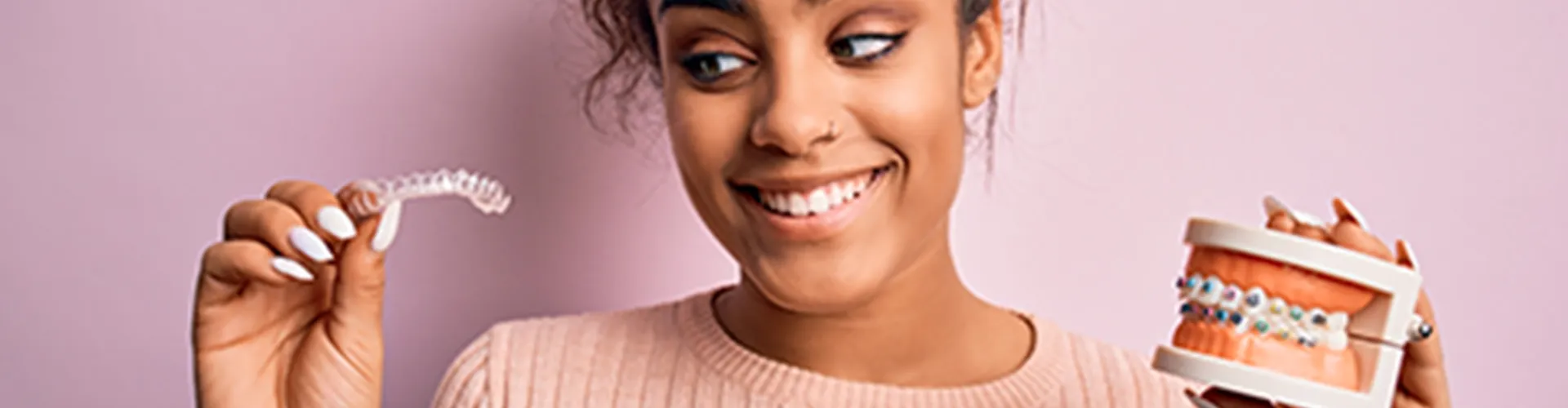 a woman holding clear alginer and a denture with braces.