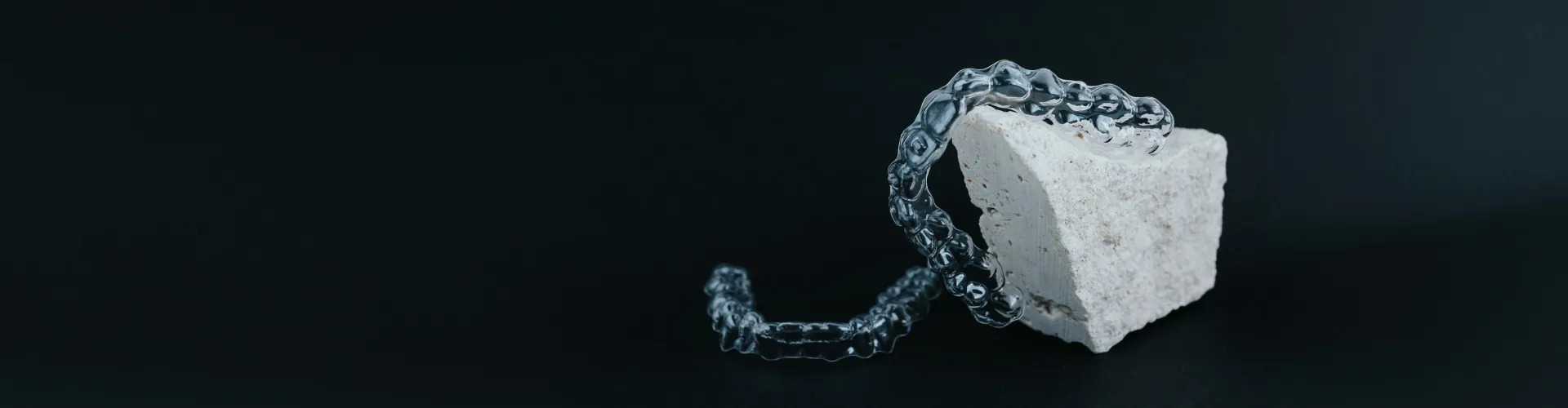 Two clear aligners on a black surface with a white rock.