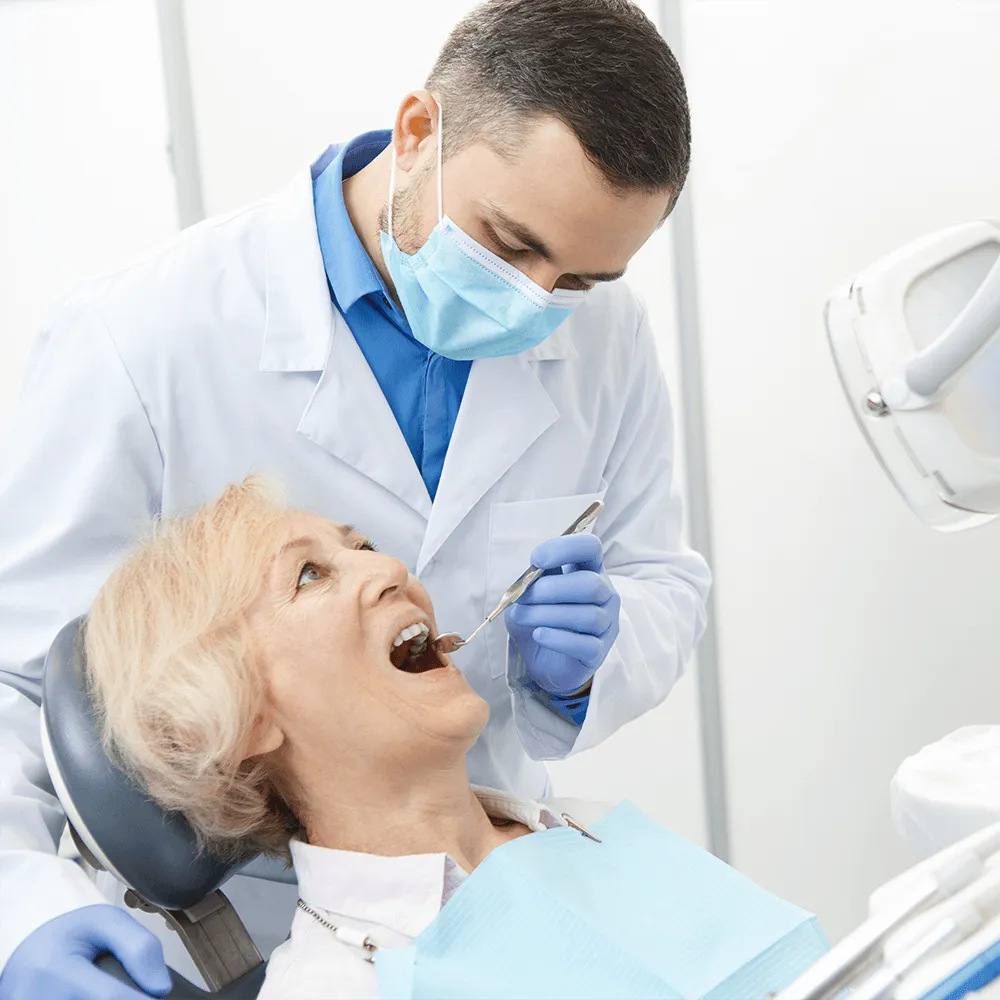 Dentist examining senior patient's teeth with a dental mirror.
