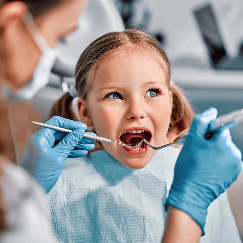 Pediatric dentist examining a young girl's teeth with dental tools.