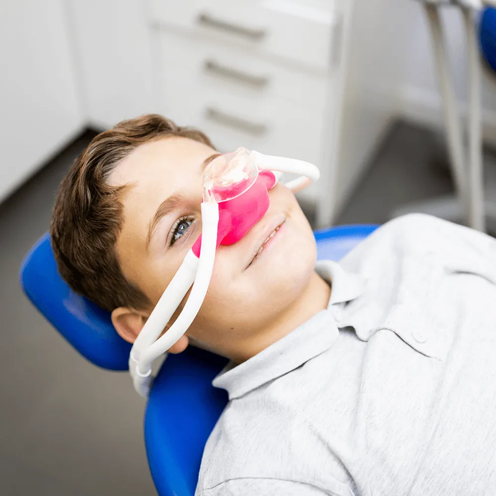 Boy relaxed in dentist chair, wearing nitrous oxide mask for comfortable dental procedure.