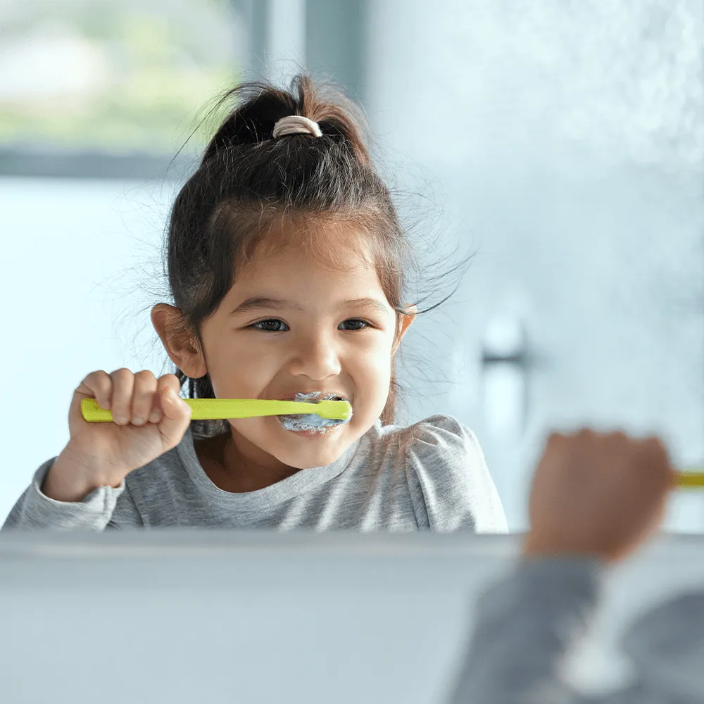 Happy little girl brushing her teeth with a bright yellow toothbrush.