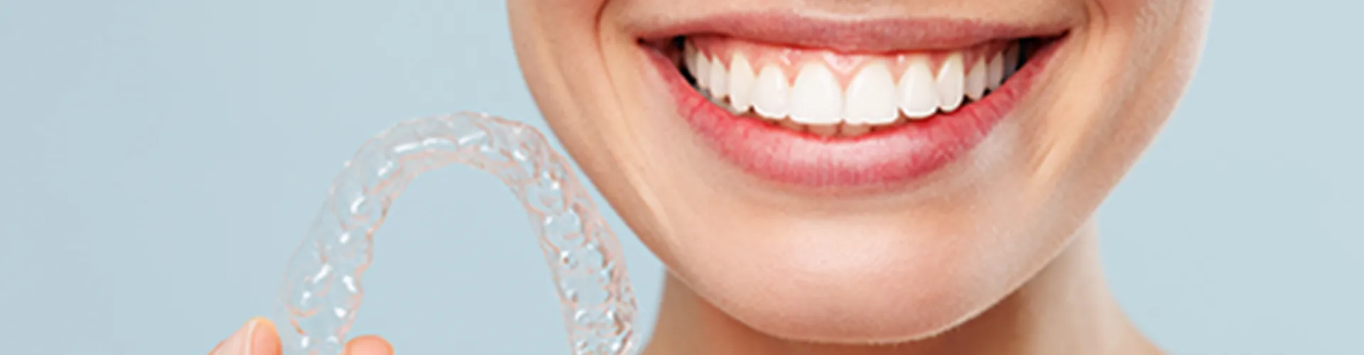 Smiling woman holding clear aligner.