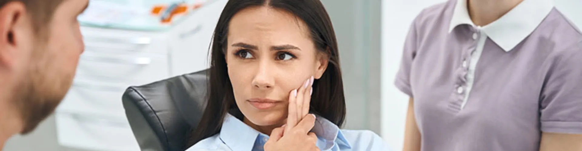 Female patient holding her cheek and looking at male dentist.